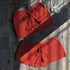 Red crochet bikini cover-up shorts with tassel ties, displayed on wooden background with flowers