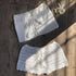 White crochet bikini skirts with drawstrings and tassels, laid on wooden surface