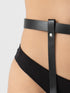 Close-up of a model's lower torso wearing a black faux-leather garter belt with a vertical strap and silver-tone rivet, paired with black underwear against a light gray background.