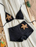 Black textured bikini set with starfish appliqués, laid flat on a cream knit blanket with beach-themed props.