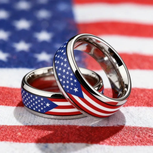 Two metallic rings with an American flag design, featuring a blue field with white stars and red and white stripes, displayed on a red, white, and blue American flag background.
