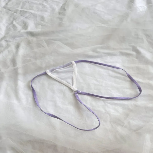 A delicate lavender and white strappy jewelry accessory, possibly a small necklace or pendant, laid flat on a textured white fabric background.