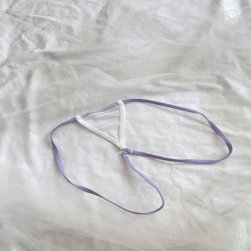 A delicate lavender and white strappy jewelry accessory, possibly a small necklace or pendant, laid flat on a textured white fabric background.