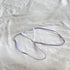 A delicate lavender and white strappy jewelry accessory, possibly a small necklace or pendant, laid flat on a textured white fabric background.